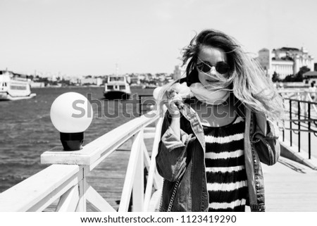 Black-and-white portrait of a beautiful young girl wearing sunglasses outdoors, woman in sunglasses walking near the sea, emotional portrait, fashionable girl relaxing on the dock