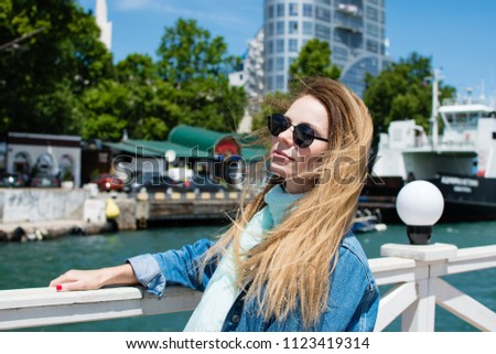 Bright portrait of a beautiful young girl in sunglasses outdoors, woman in sunglasses walking near the sea, emotional portrait, fashionable girl resting on the dock
