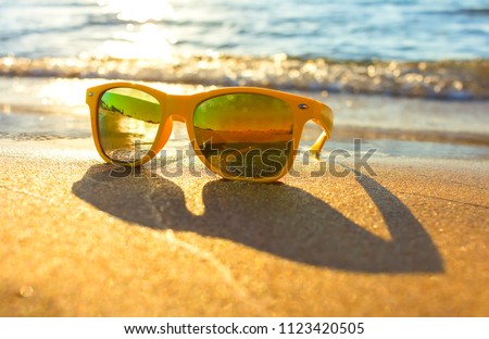 Sun glasses on beach near the sea. Yellow sunglasses on the background of sea wave on the shore of a tropical island. Depth of field blur