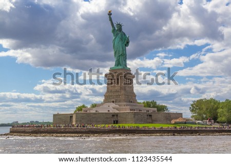 Color landscape photo of the Statue of Liberty on Ellis Island, New York, USA. Statue is in center of frame with copy space in cloudy sky. 