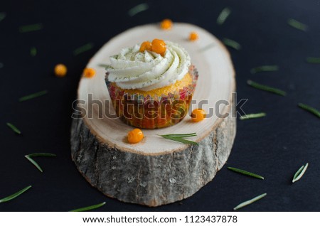 Cupcake with seaberry on wooden plank decorated with rosemary on black background
