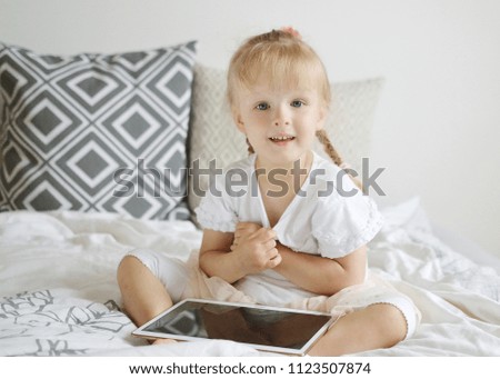 Caucasian Little Blond Girl Playing Tablet Games in Bed, Home Interior, Modern Device Technologies Scandinavian Style