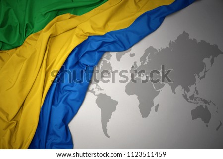 waving colorful national flag of gabon on a gray world map background.