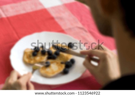 Man sitting at the table with cloth and eats pancakes with blackberries. Blurred background.