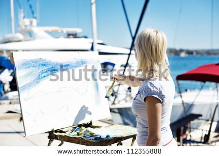 Beautiful blonde on the beach draws,a young girl painting a picture