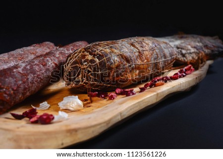 Horizontal pic of ham and sausage with decoration on wooden cutting board. Black backgound. concept