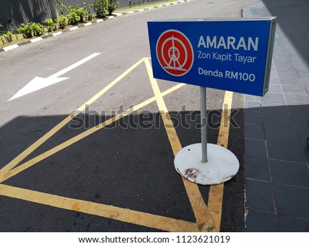 Outdoor sign board word - WARNING WHEEL CLAMPING ZONE RELEASE FEE RM100 or AMARAN ZON KAPIT TAYAR DENDA RM100 in Malaysia Language appear at the road.