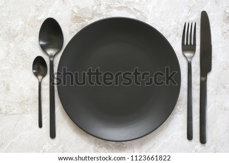 Black silverware and empty plate on marble. Top view point.
