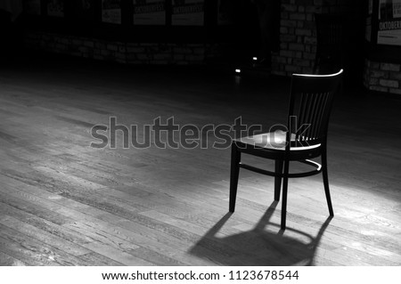 A wooden chair standing in the middle of an empty stage under the light of soffits, in black and white Royalty-Free Stock Photo #1123678544