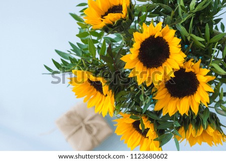 Bouquet of bright sunflowers with gift on a white table.