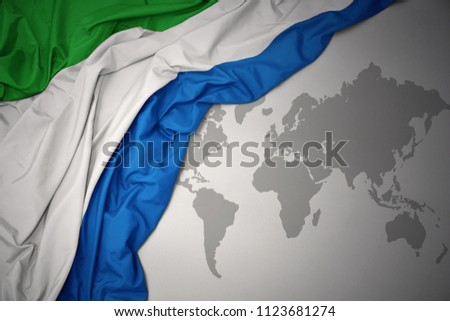 waving colorful national flag of sierra leone on a gray world map background.