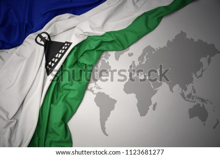 waving colorful national flag of lesotho on a gray world map background.