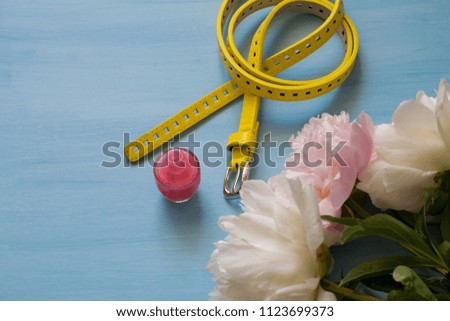 Delicate white and pink peonies, nail polish and yellow leather belt on a blue background