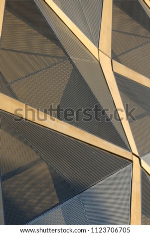 Close up outdoor view of part of a modern building facade made of brown decorative lozenges. Pattern of lines and polygonal shapes with shadows. Abstract architectural design of a wall with reliefs.