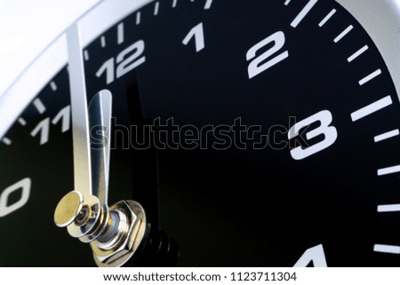 Closeup of modern black chrome clock on white background indicates twelve o'clock, wake up, time for action, time up or midday. Time passing concept for business urgency and running out of time.