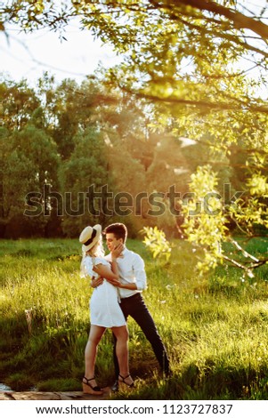 Handsome guy and blonde girl walking on the field of wheat on a beautiful warm sunset. gently hug, standing in the sun
