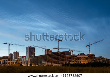 Night sky view of beautiful noctilucent clouds over the city. Cityscape of house building with construsction cranes. Rare phenomena which happens only on summer nights. Cityline with cloudy sky Royalty-Free Stock Photo #1123732607