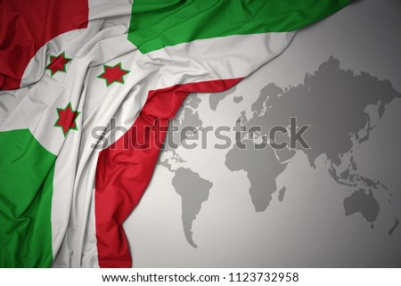 waving colorful national flag of burundi on a gray world map background.