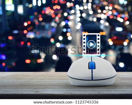 Play button and movie icon with wireless computer mouse on wooden table over blurred colourful night light city with cars, Cinema online concept