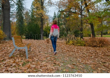  girl is walking in the autumn park.  tourist woman walks with a backpack over an autumn park with fallen leaves
