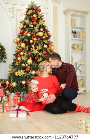 Little european daughter sitting with father and pregnant mother near Christmas tree and keeping gifts. Concept of winter holidays and happy family.