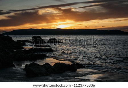 Beautiful sunset with dramatic clouds on Adriatic Sea coast.Sun goes down over horizon behind mountains on exotic tropical island in Croatia.Travel destination for summer vacation cruise