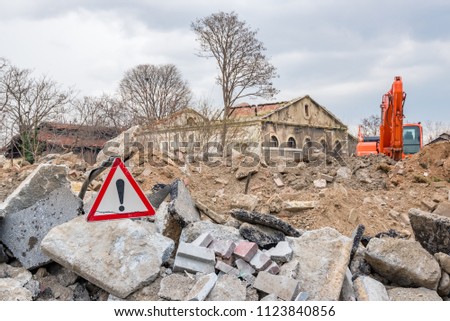 Red traffic triangle warning sign stands in front of destroyed building.Hazard warning attention sign with exclamation mark symbol