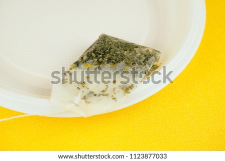 used tea bag on plastic plate on yellow background