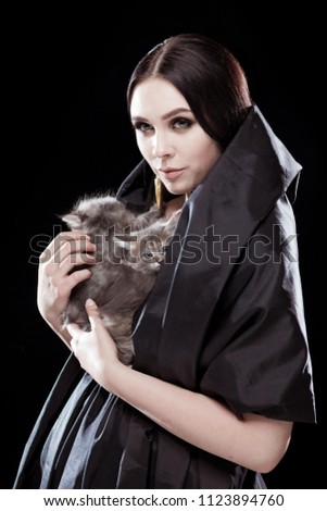 Portrait of a young girl in a black raincoat holding a kitten in her arms