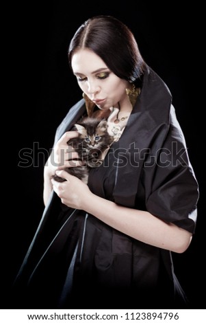 Portrait of a young girl in a black raincoat holding a kitten in her arms