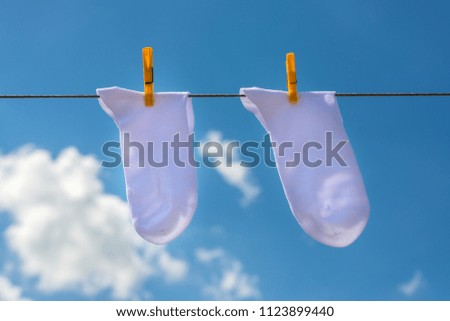 Two new, clean, washed white socks hang on a rope with yellow clothespins. blue sky background with clouds