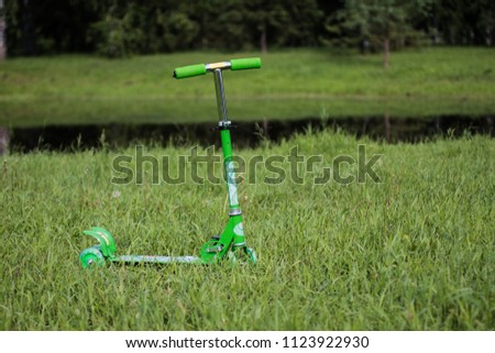 children's green scooter in the grass near the lake in the Park