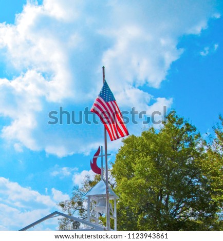 American flag against the blue sky, green tree and church cross.
Traditional symbol of America in a bright sunny summer day in the Edom, near Tyler in Texas. 