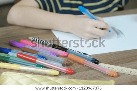 Close-up of the child's hands paint the picture with a blue felt pen on white paper. Side view.