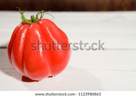 wet, fresh buffalo heart tomato on the left side of the picture, on white woden board