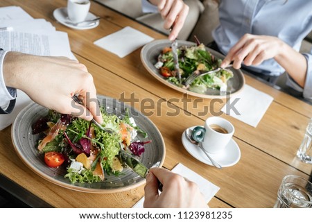 Man and woman having business lunch at restaurant sitting at table eating two plates of fresh vegetable salad close-up Royalty-Free Stock Photo #1123981235