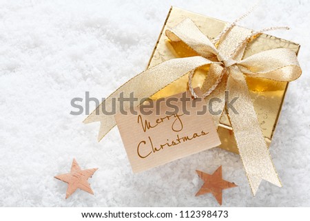 Gold gift with a decorative ribbon and Merry Christmas tag nestling on fresh snow with stars and copyspace