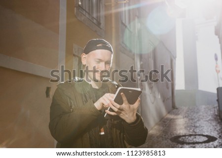 A young male tourist on the street uses a tablet to look at an application with maps of the area or call a taxi or something else