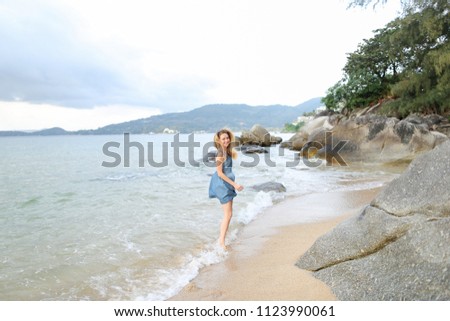 Young european girl wearing jeans sundress and walking barefoot on sand, morning sea shore. Concept of tropical summer vacations and resting.