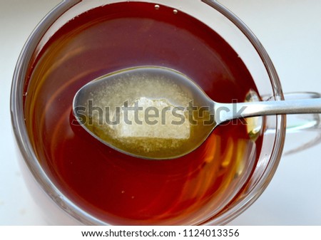 Transparent cup of black tea with a teaspoon in which sugar dissolves. Top view