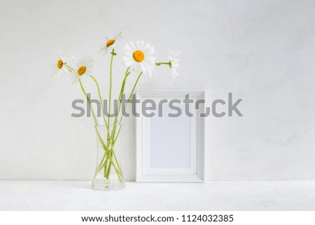 Mockup with a white frame and white daisies in a vase on a light background