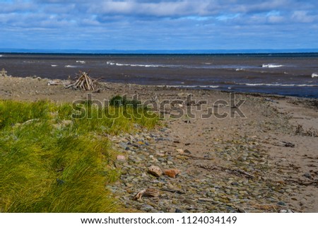 A view of the beach on Miscou Island on Prince Edward Island, Canada with cairns and piled tree branches on the shore