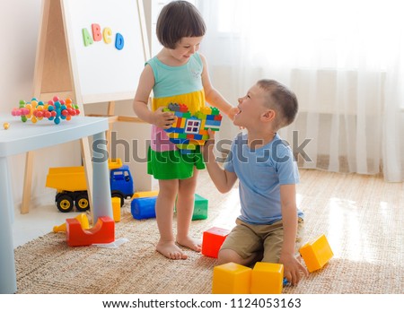 A boy and a girl are holding a heart made of plastic blocks. Brother and sister have fun playing together in the room. Preschool children and educational toys Royalty-Free Stock Photo #1124053163