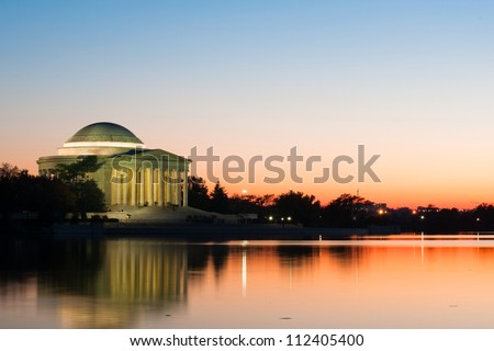 Peaceful view of Jefferson Memorial at sundown with distant city lights and soft reflections on calm, still water. Taken at Tidal Basin, Washington DC early fall.