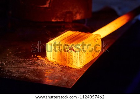 Glowing iron ingot on the table. Hot metal workpiece for the manufacture of Damascus steel. Royalty-Free Stock Photo #1124057462