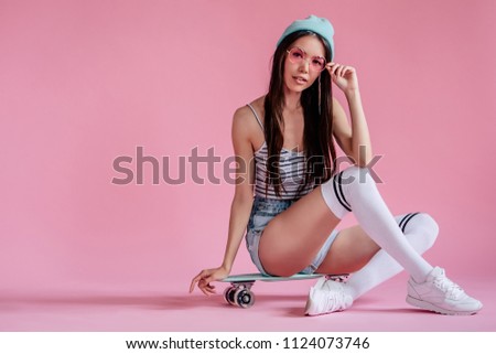 Young asian teenage girl on pink background with pink glasses. Skater girl in shorts with skateboard isolated.