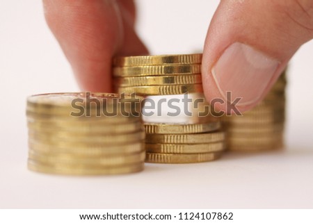 Fingers taking or placing golden coins from stac or piles of money. Close up og hand and money piles with selective focus.