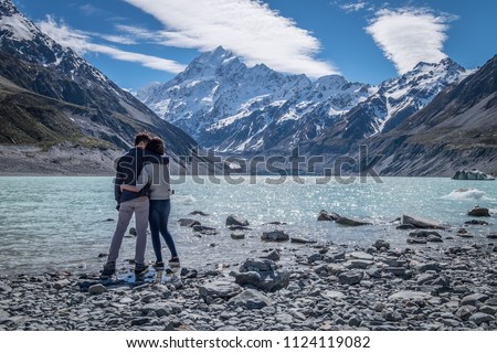 A young romantic couple admiring the beautiful scenery of mount cook in New Zealand. The rocky shore, stunning snow mountain and the clear sky create a perfect background or wallpaper. Royalty-Free Stock Photo #1124119082