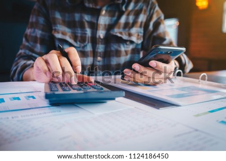 Business man holding pen and using smartphone for calculating financial marketing with calulator at workplace. Business finances and accounting concept. Royalty-Free Stock Photo #1124186450