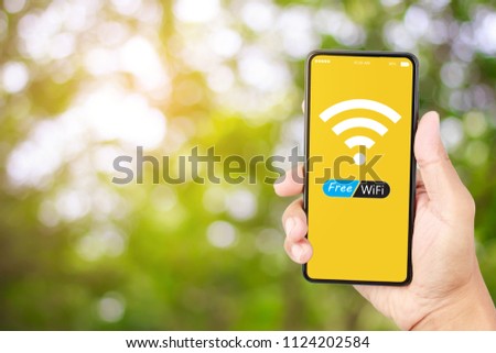 Hand holding smart phone with free wifi on yellow screen over green bokeh blur background
